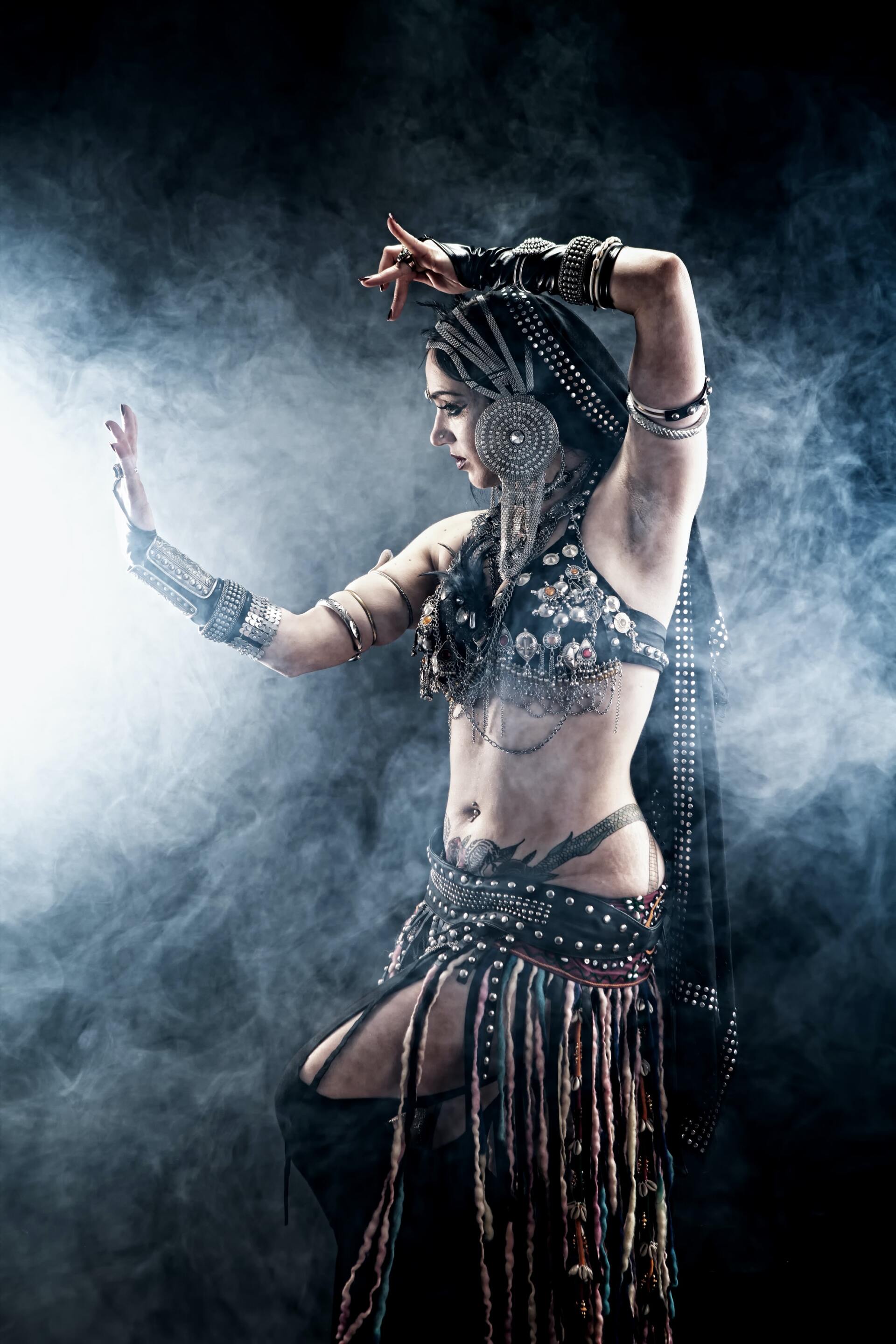 A belly dancer is dancing in front of a smokey background.