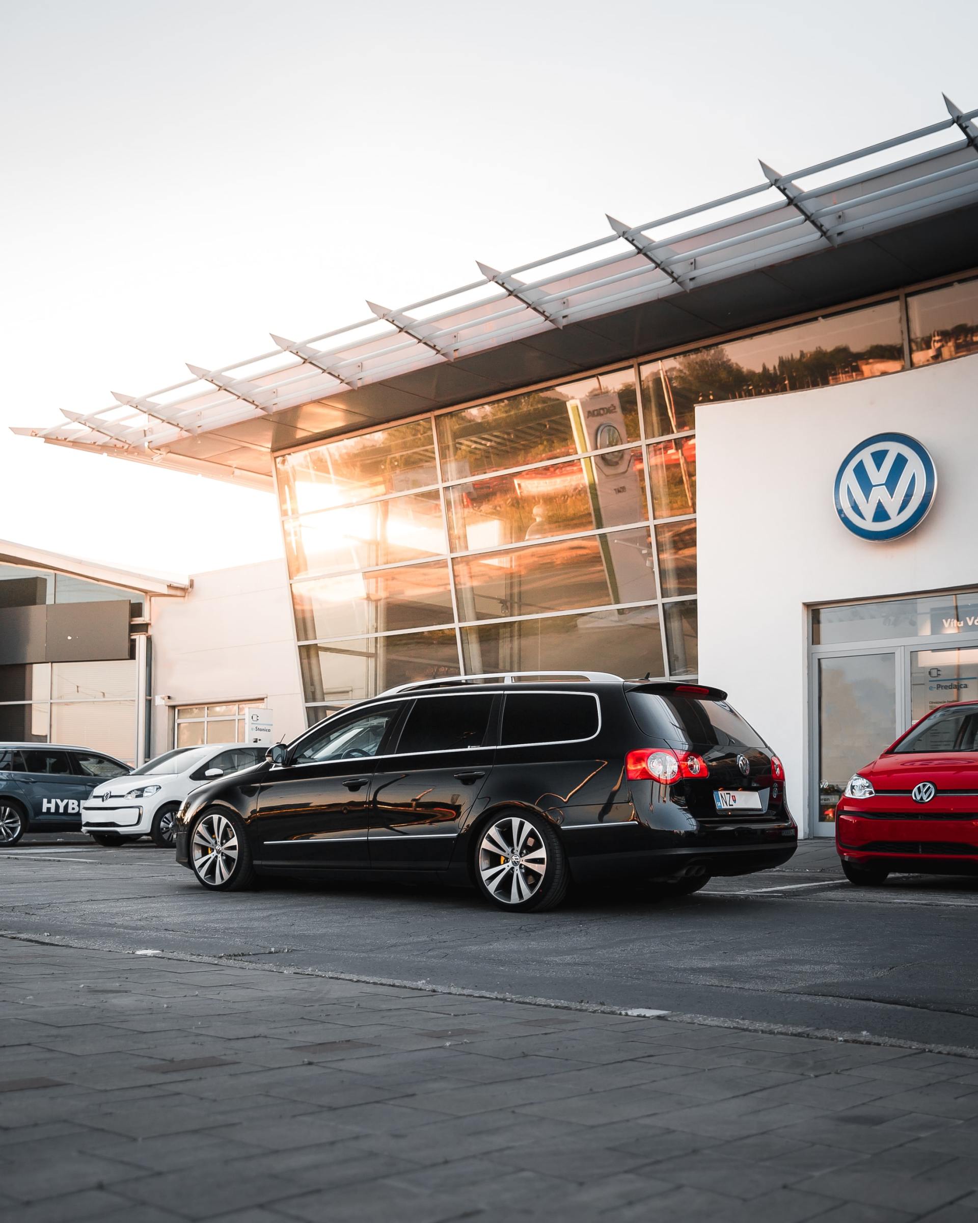 A row of cars are parked in front of a volkswagen dealership.
