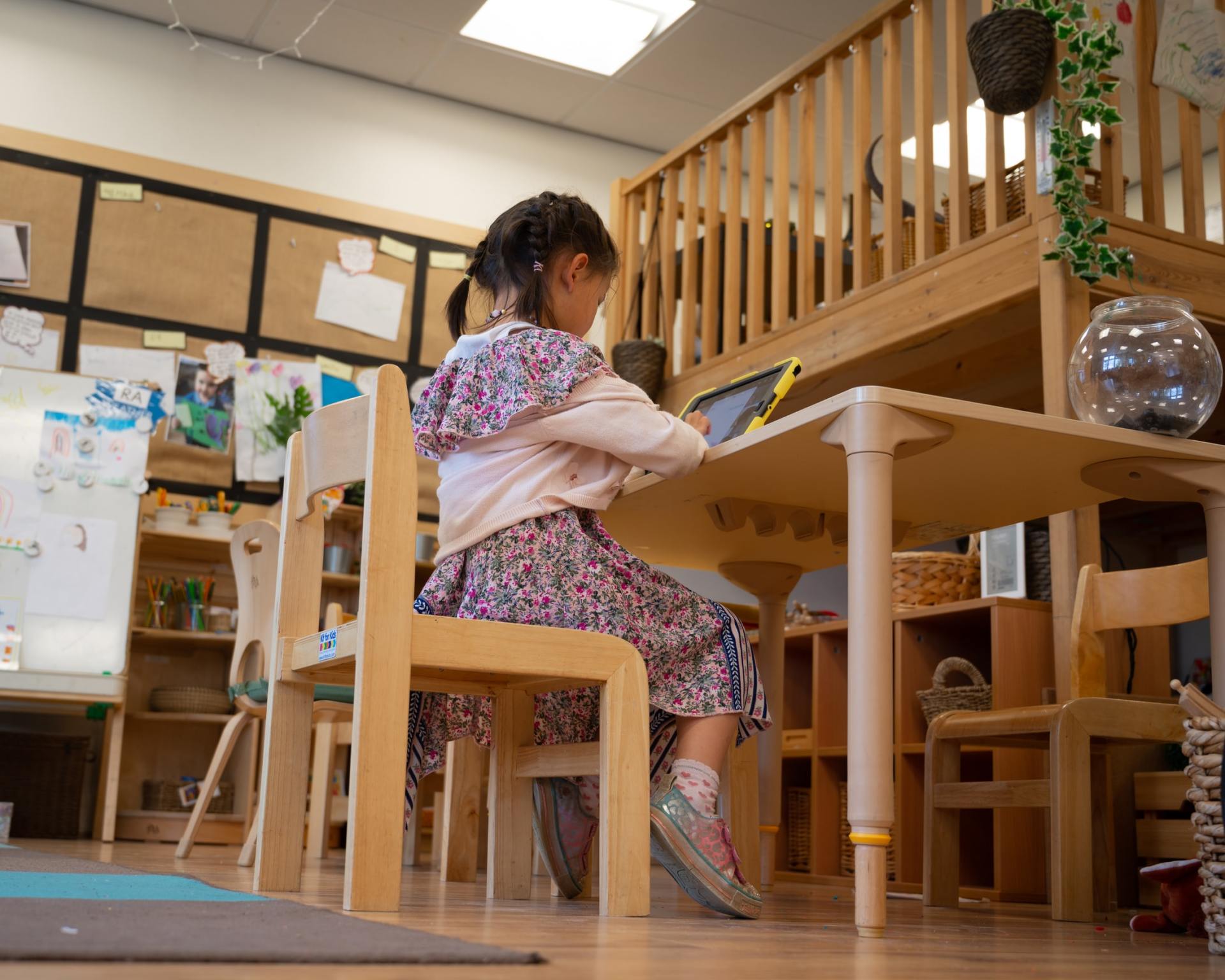 A little girl is sitting at a wooden table in a classroom.
