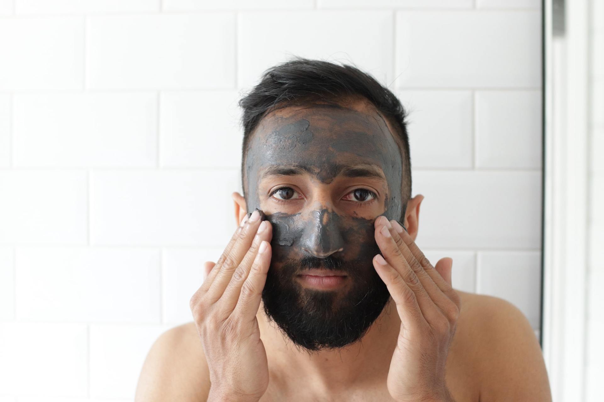 a man with a beard is applying a black mask to his face .