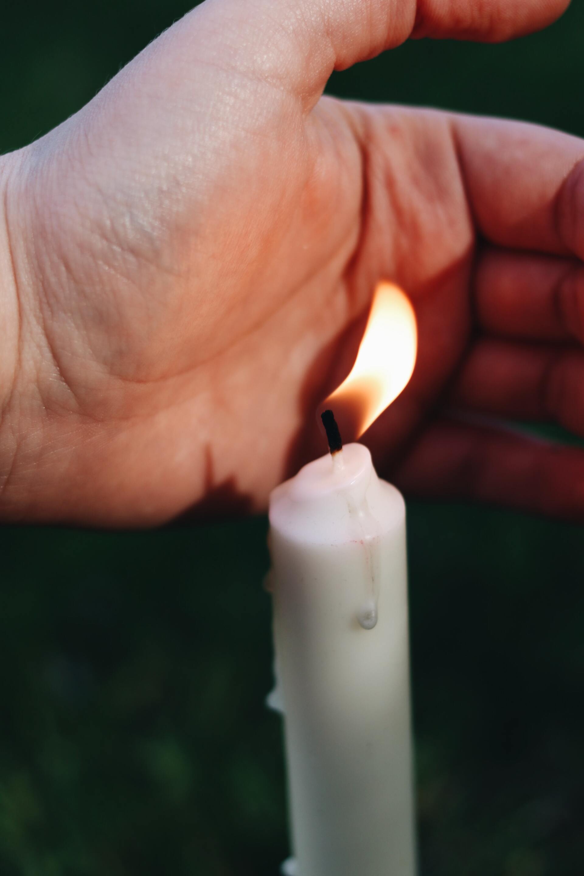 A person is lighting a white candle with their finger