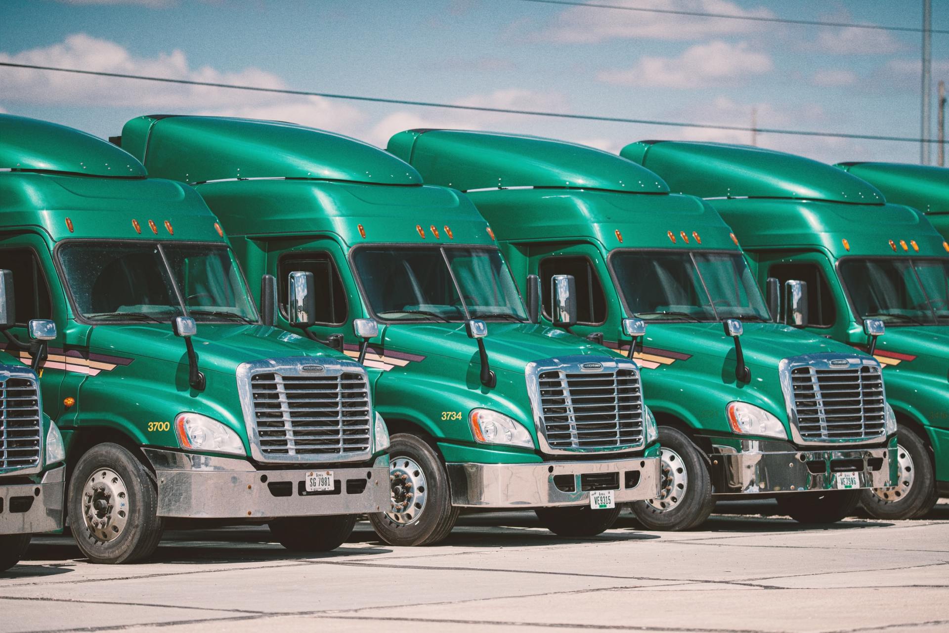 A row of green semi trucks are parked in a parking lot.