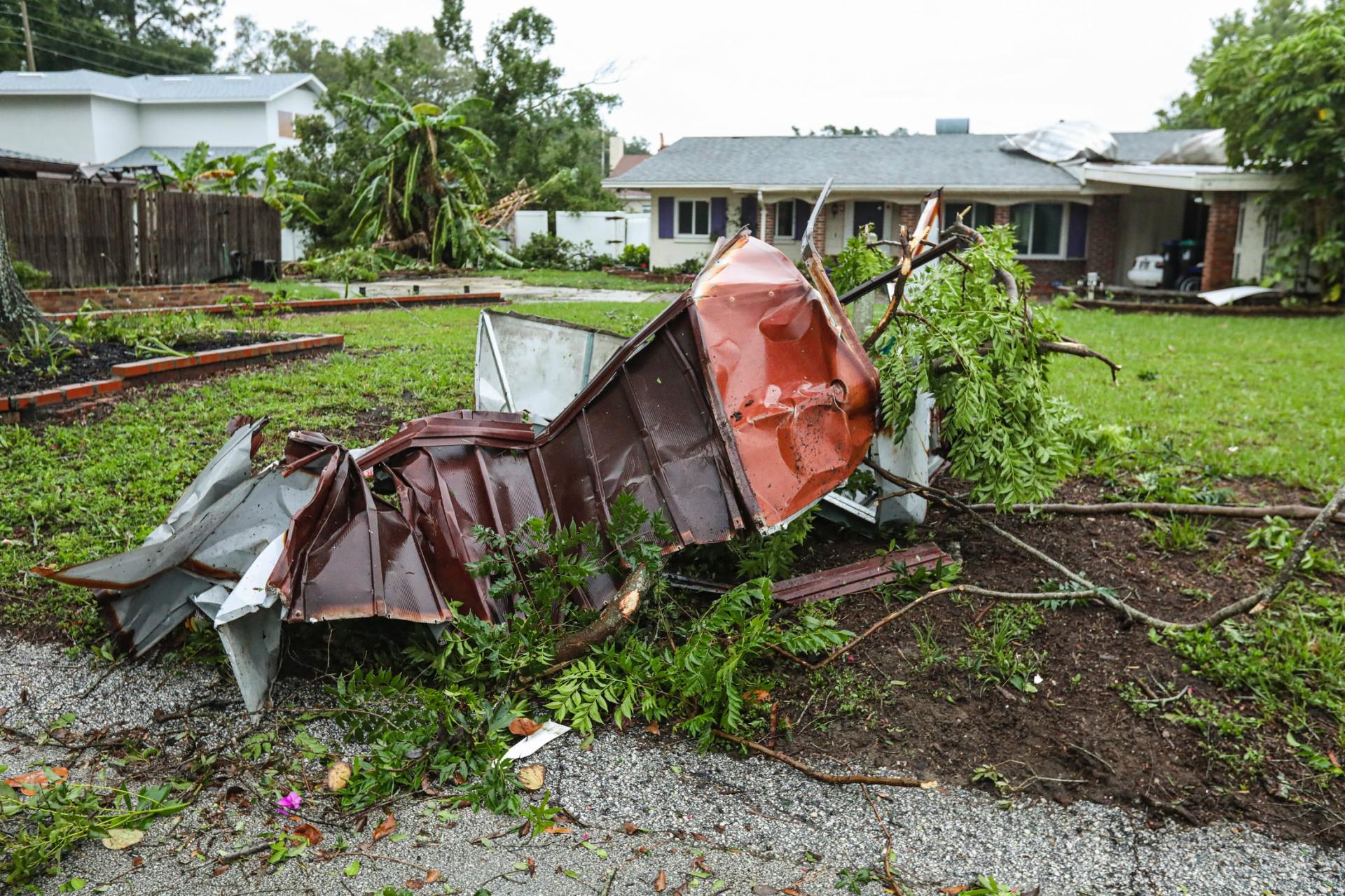 Image of tornado damage with trees and shrubs down on house and yard