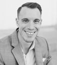 A man in a suit is smiling in a black and white photo.