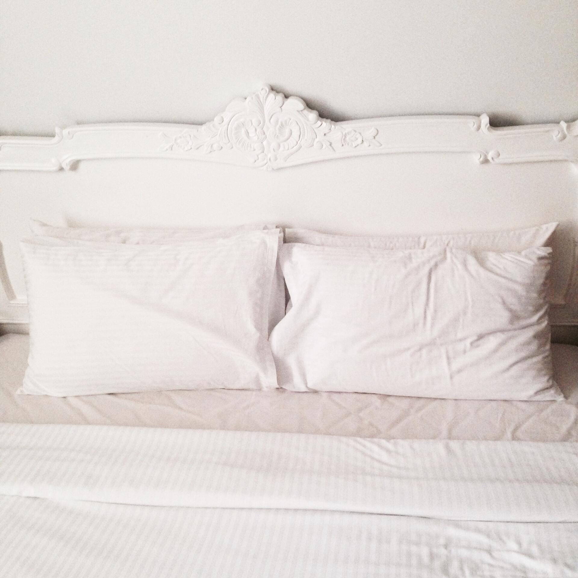 A bed with white sheets and pillows and a white headboard