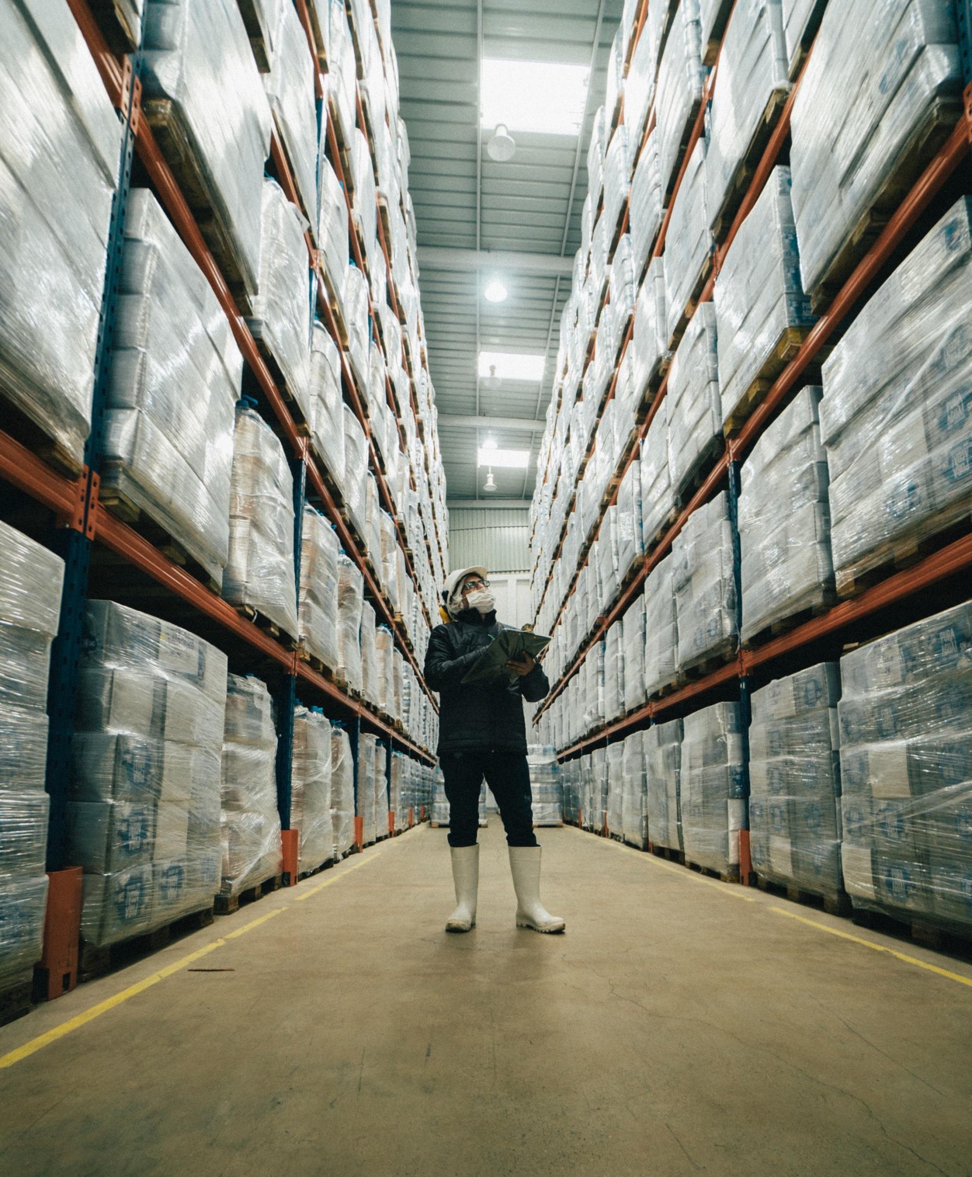 A man is standing in a warehouse looking at a clipboard.