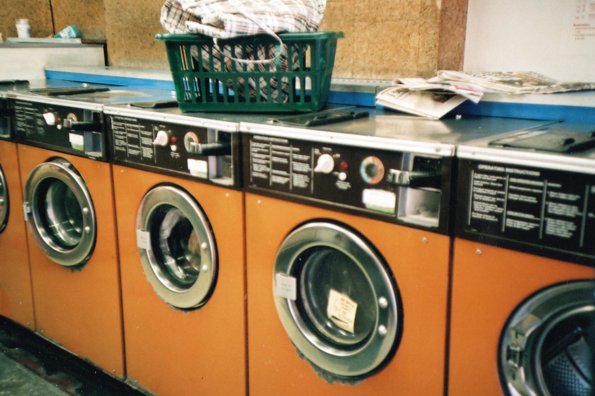 a row of washing machines in a laundromat with a basket on top of one of them .