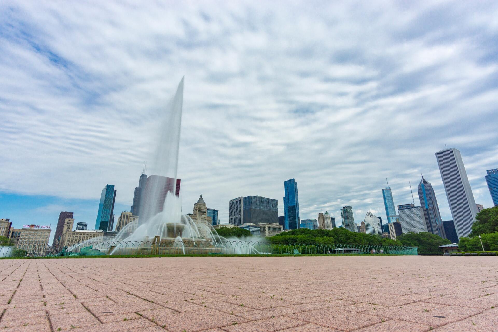 A fountain in front of a city skyline on a cloudy day.
