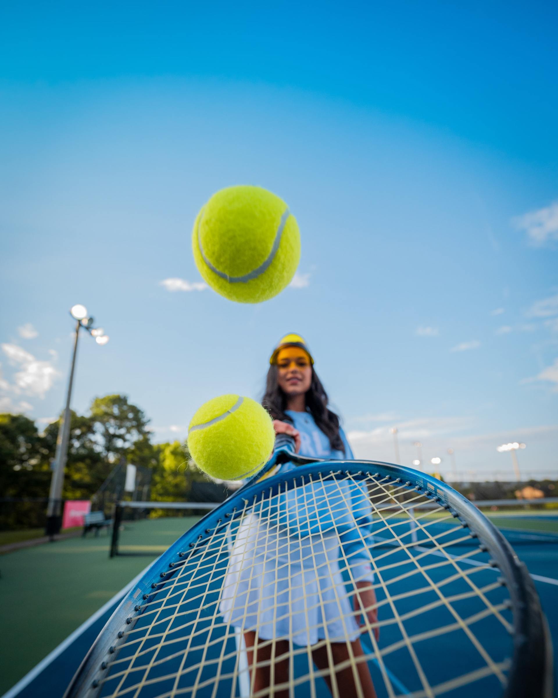 A woman is holding a tennis racket and two tennis balls are flying in the air.
