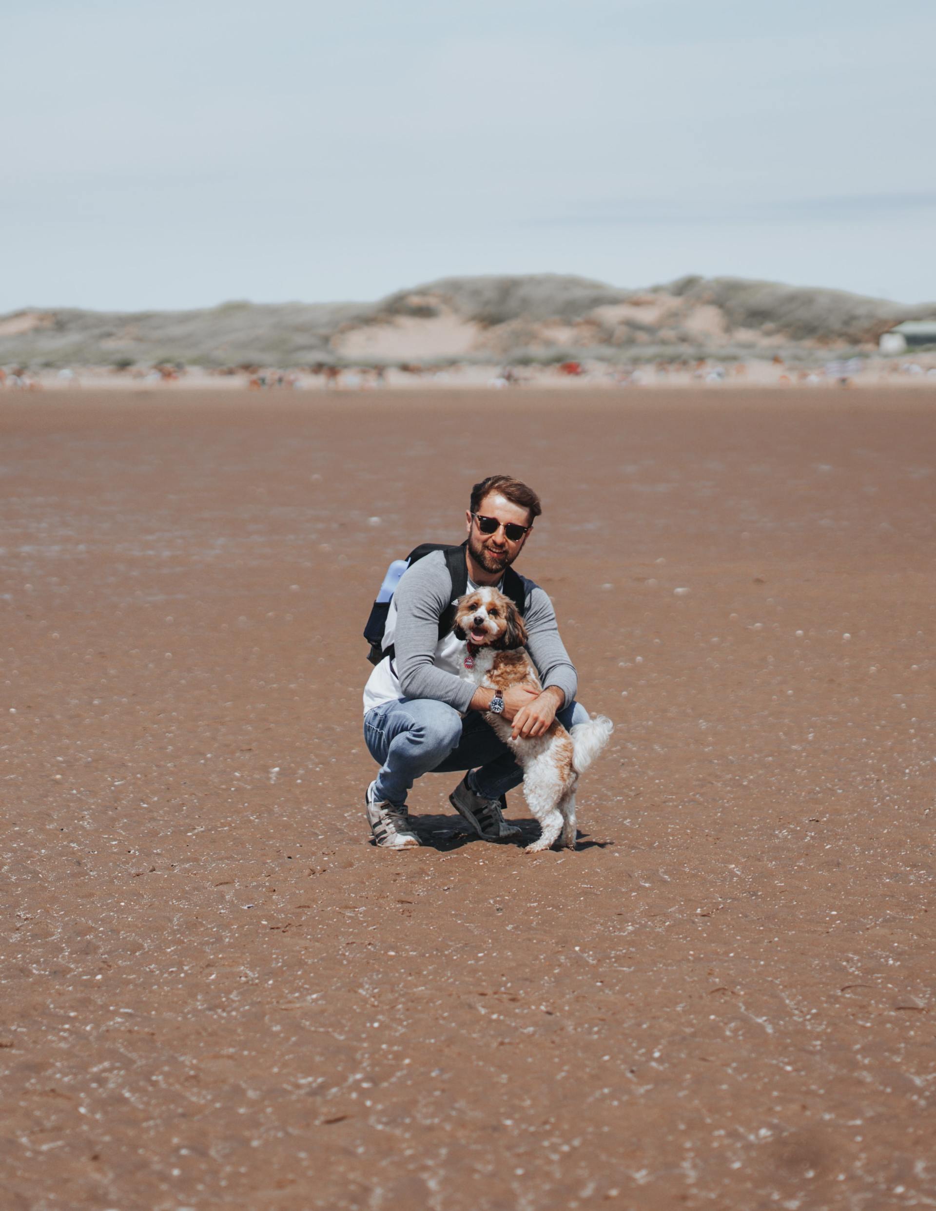 A man is kneeling down with a dog on the beach.