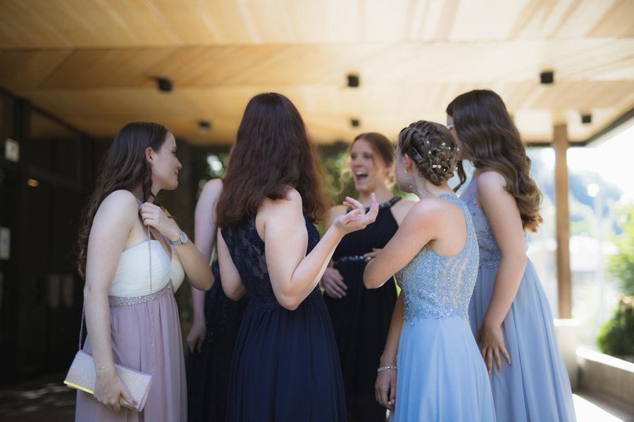 A group of women in dresses are standing around talking to each other.