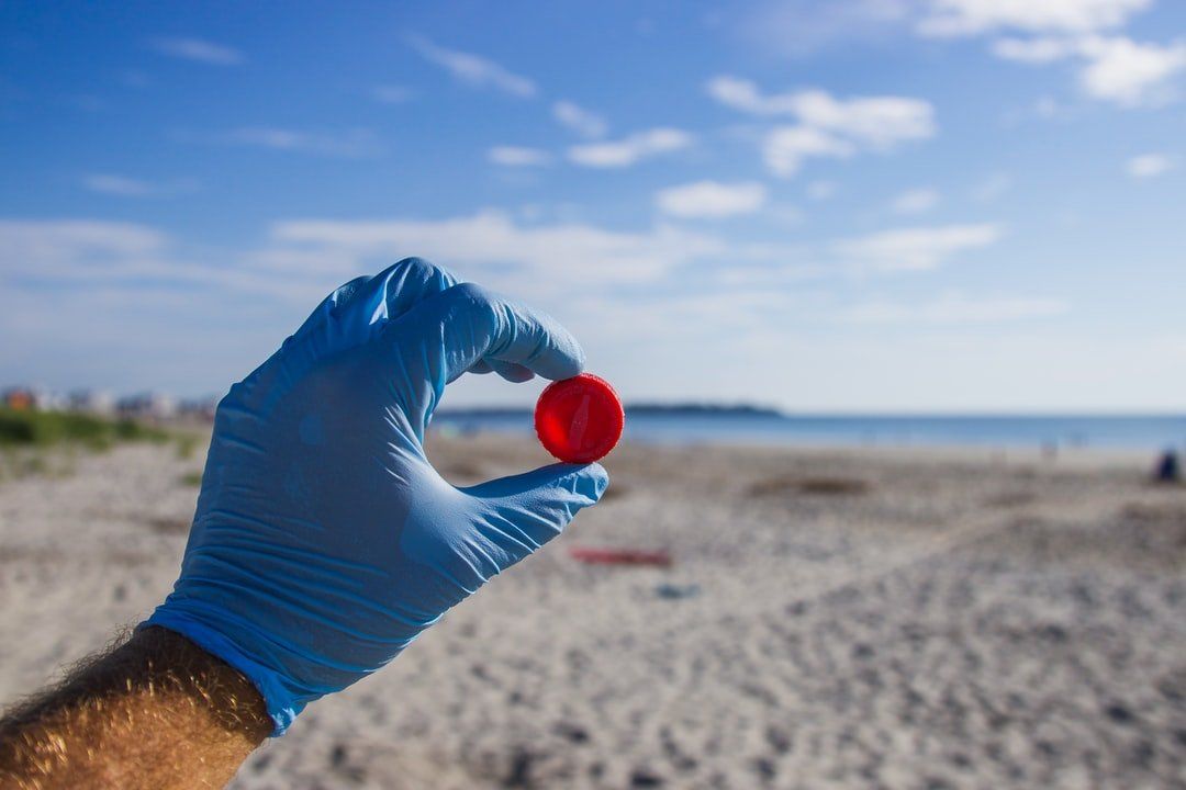 A person wearing a blue glove is holding a red ball on the beach.