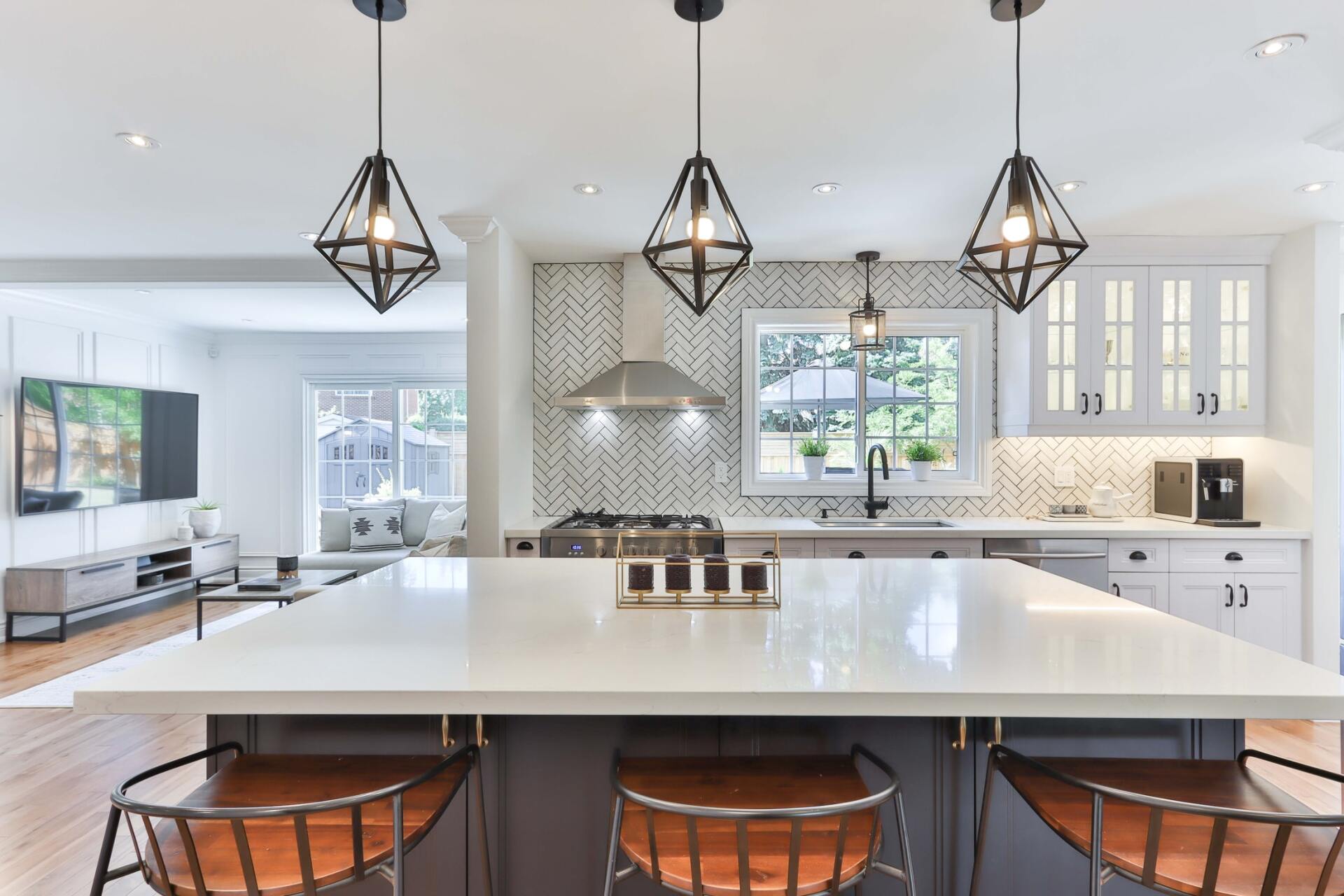A modern kitchen with herringbone subway tile, diamond pendant lights, quartz counters, and white and grey cabinets