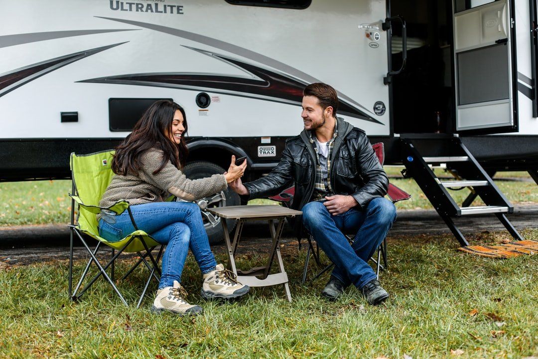 People sitting on a patio set looking at phone infront of their RV