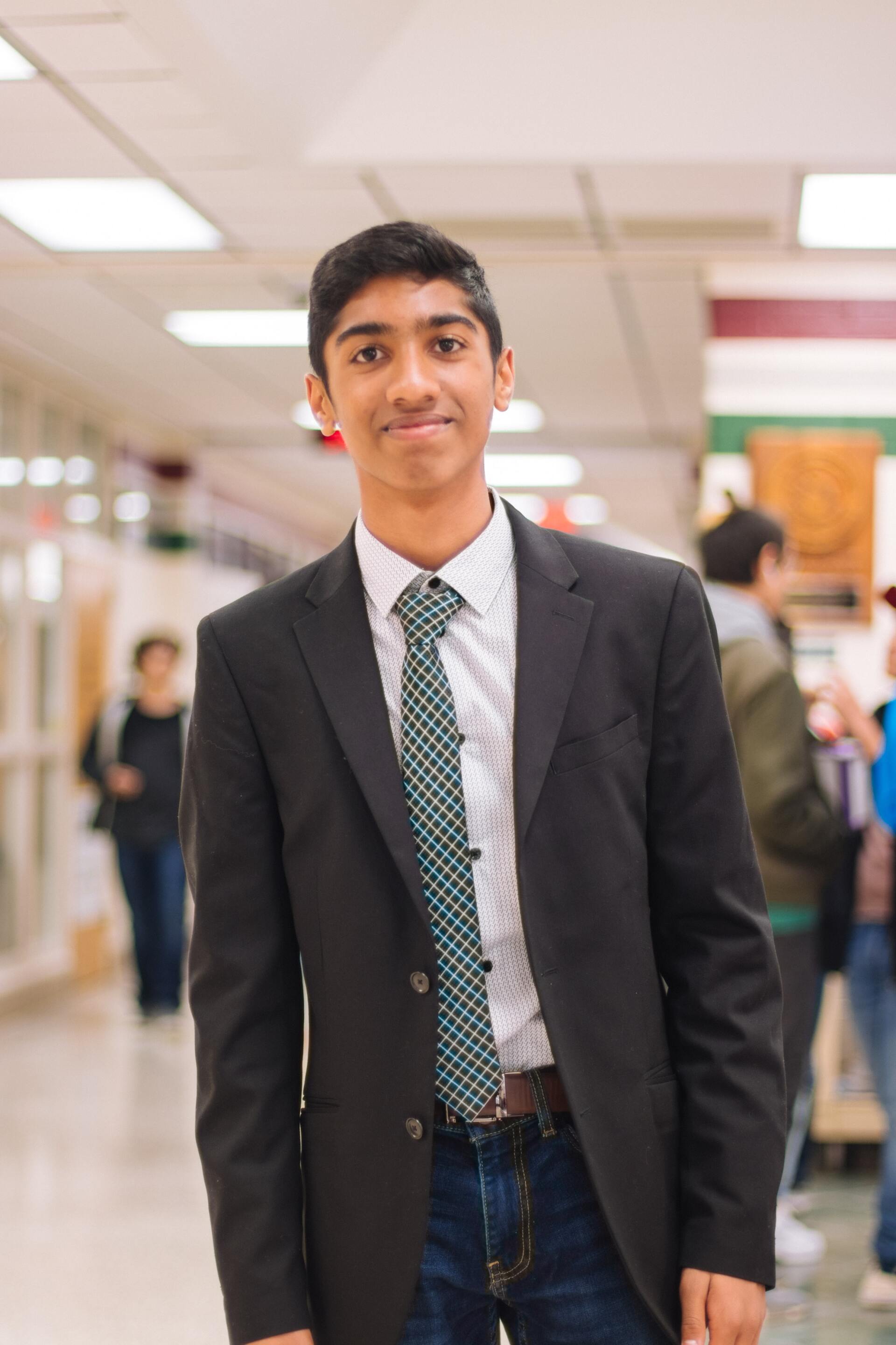 A young man in a suit and tie is standing in a hallway.