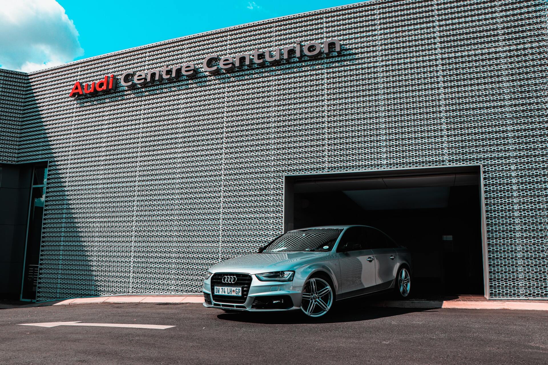 A silver car is parked in front of a building that says audi centre centurion