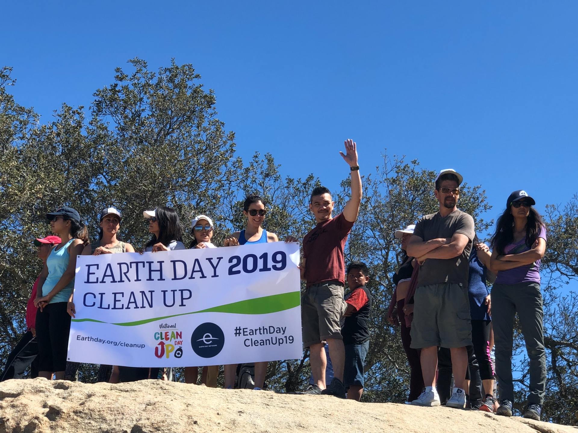 A group of people are standing on top of a hill holding a sign that says earth day 2019 clean up.