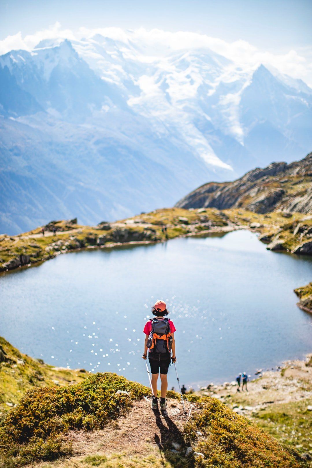 A person with a backpack is standing on top of a mountain next to a lake.