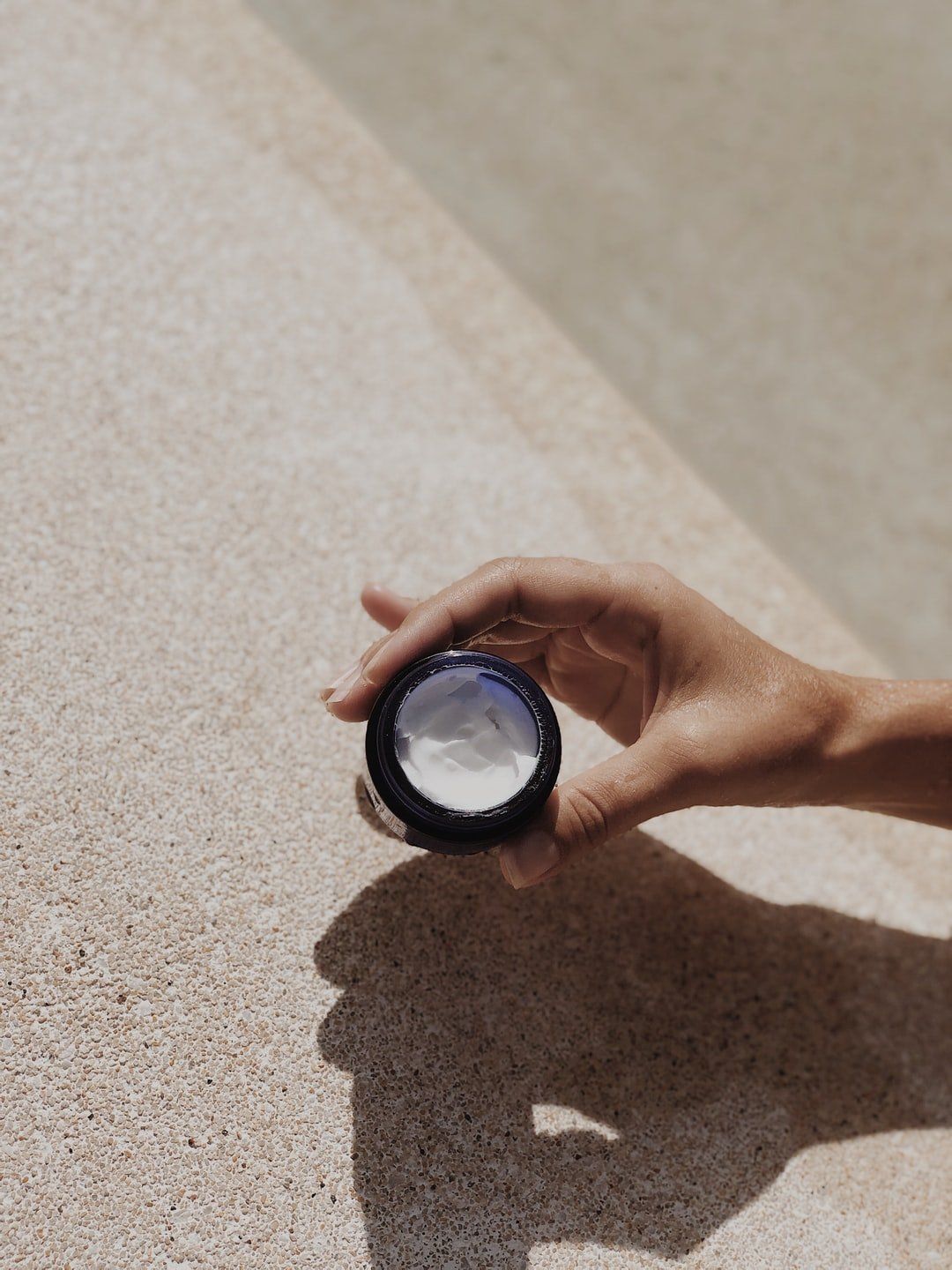 A person is holding a small jar of cream in their hand.