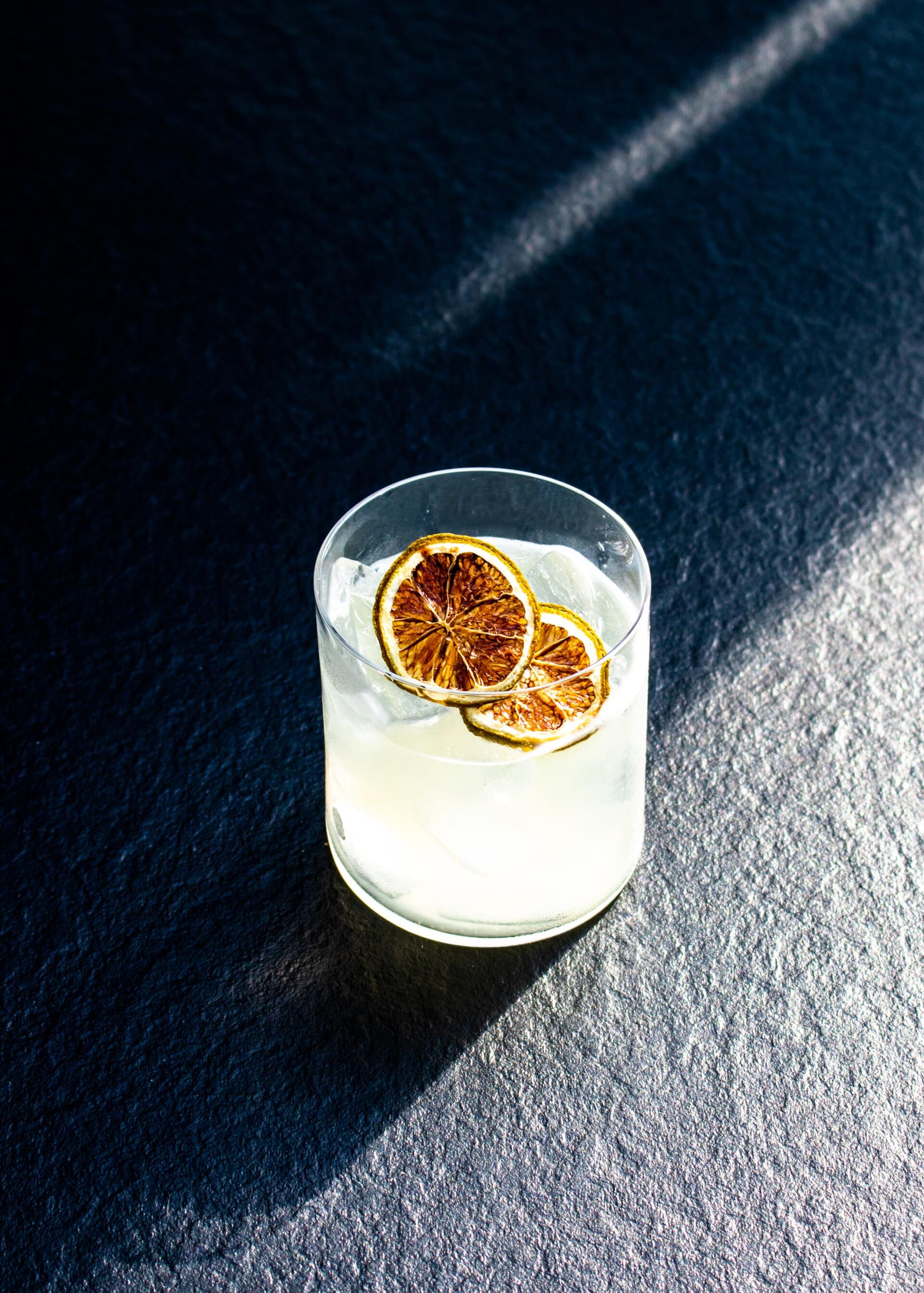 A close up of a drink with slices of orange in a glass on a table.