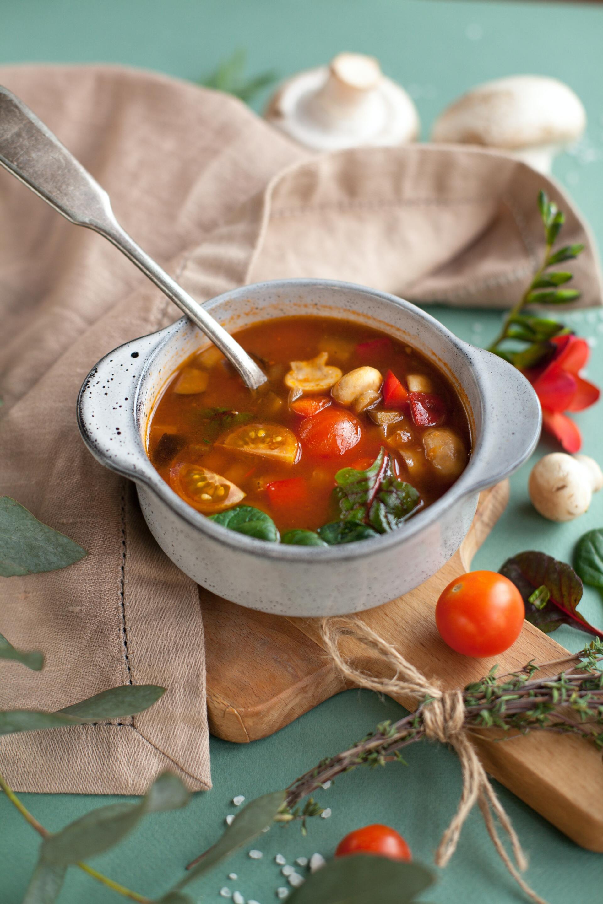 A bowl of soup with a spoon in it is on a cutting board.