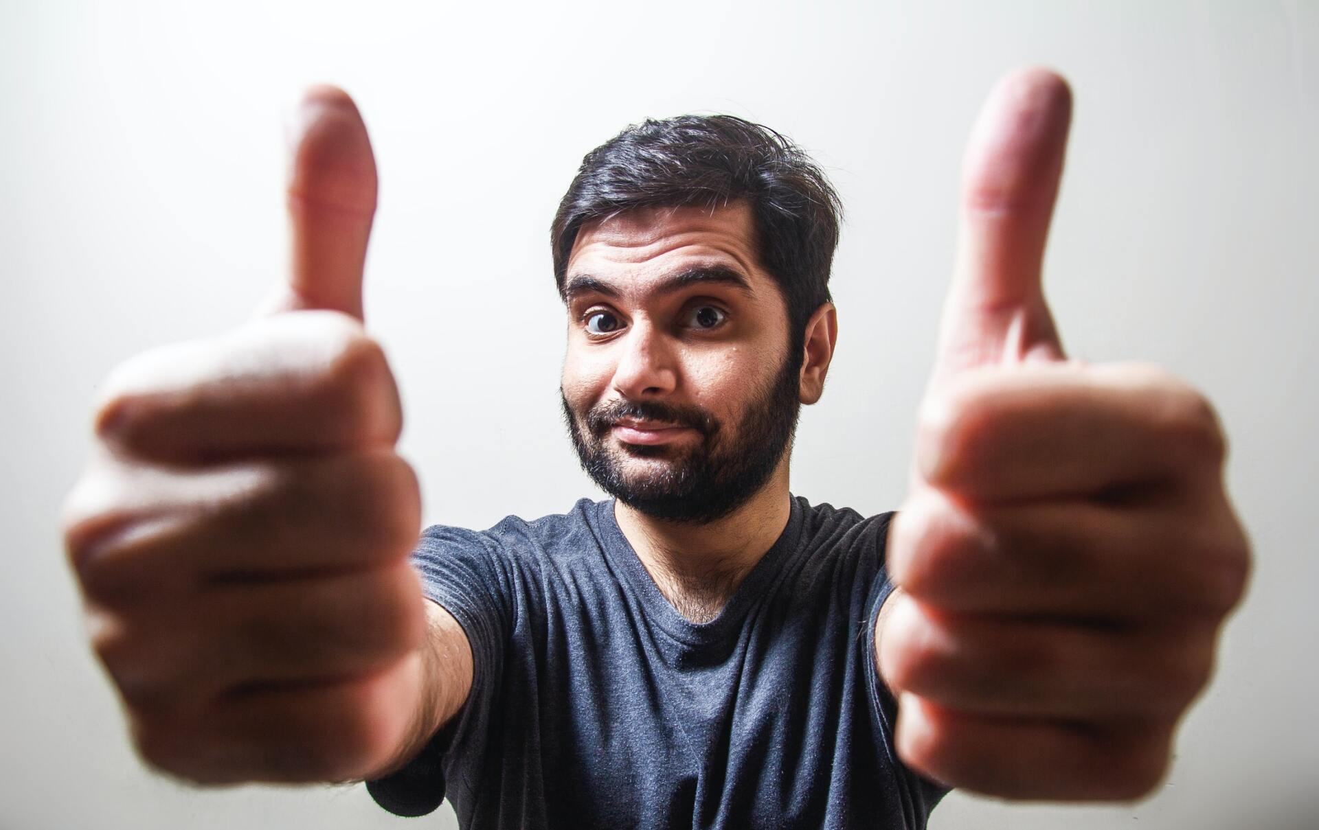 A man with a beard is giving two thumbs up.