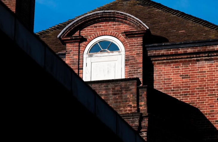 Picture of the roof on a traditional brick building by Roofing London. The roof is covered in rosemary clay tiles and there is an arched window at roof level.