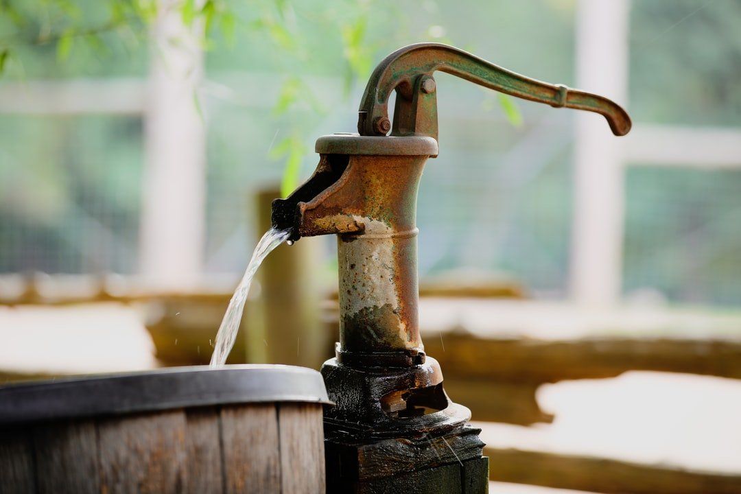 A water pump is pumping water into a wooden barrel.