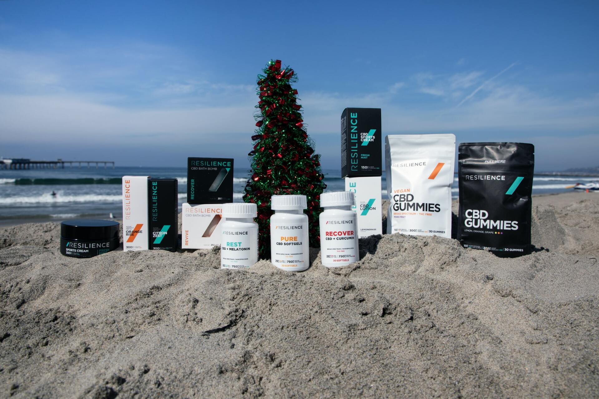 CBD supplements in plastic bottles and bags on a beach with a Christmas tree in the background.