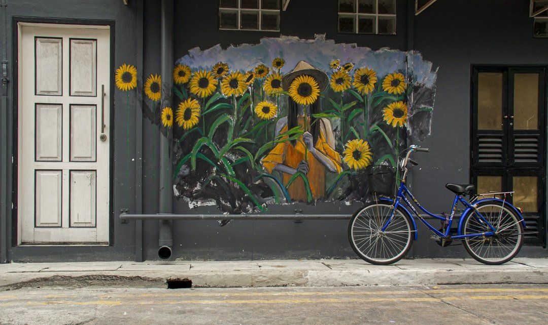 A blue bicycle is parked in front of a mural of sunflowers on a wall.