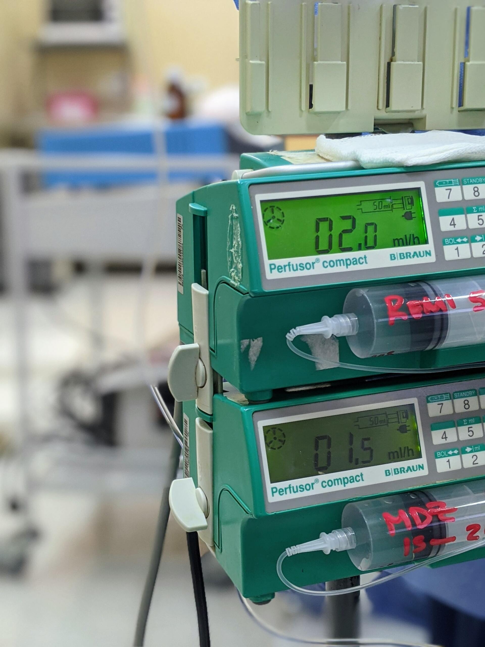 A stack of infusion pumps with syringes attached to them in a hospital room.