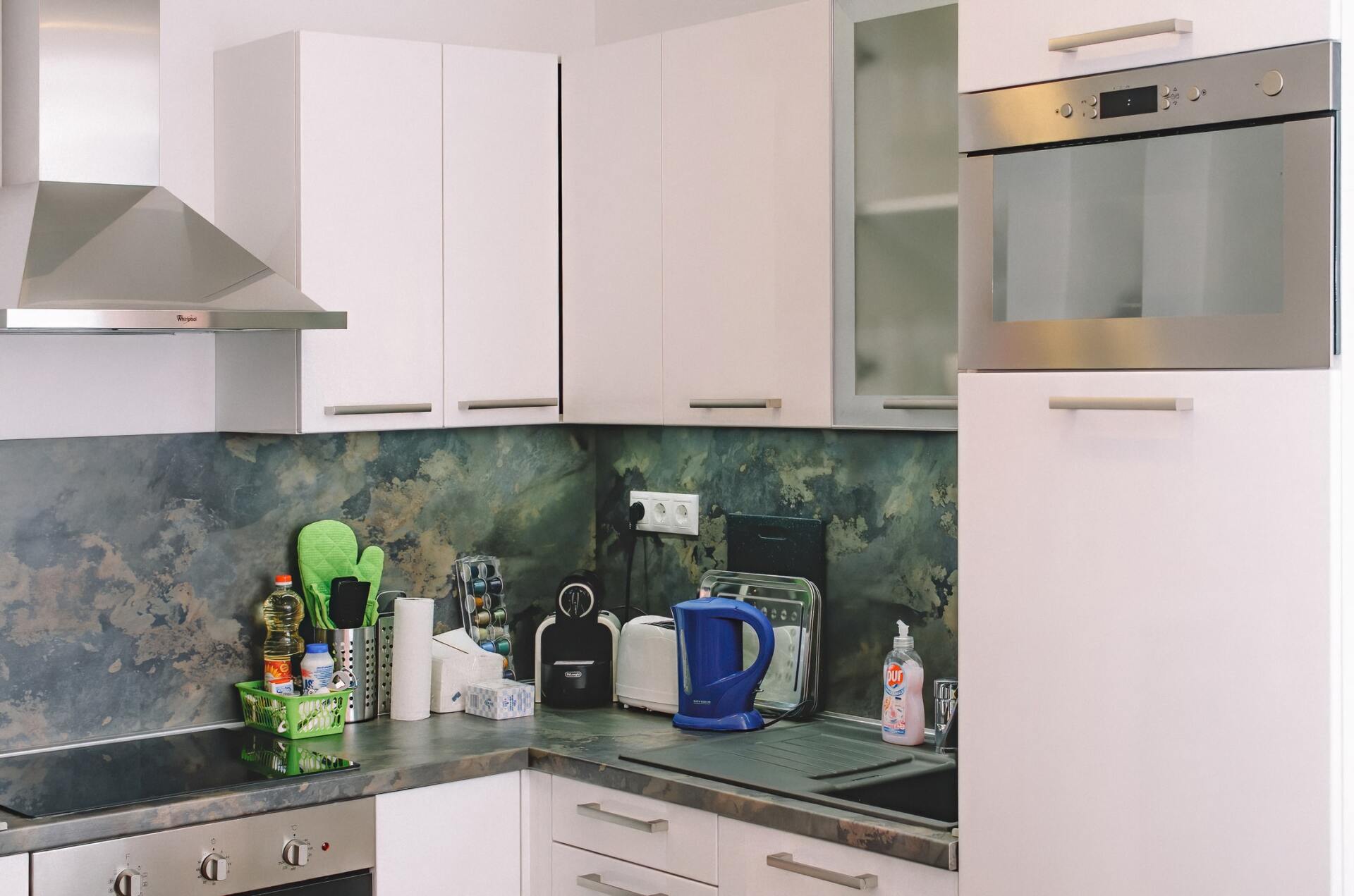 White kitchen with stainless steel oven, cabinets, and appliances; blue kettle and black countertop.