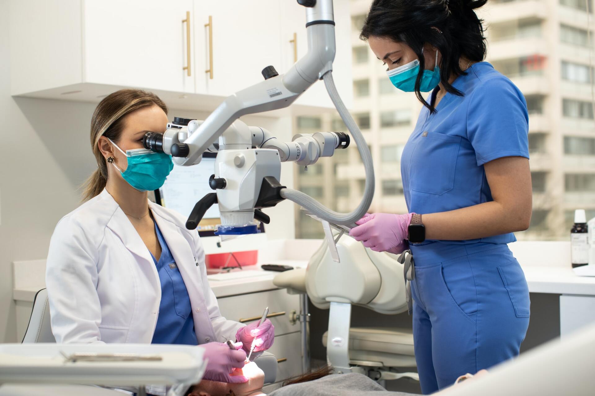 A dentist and a nurse are examining a patient 's teeth with a microscope.
