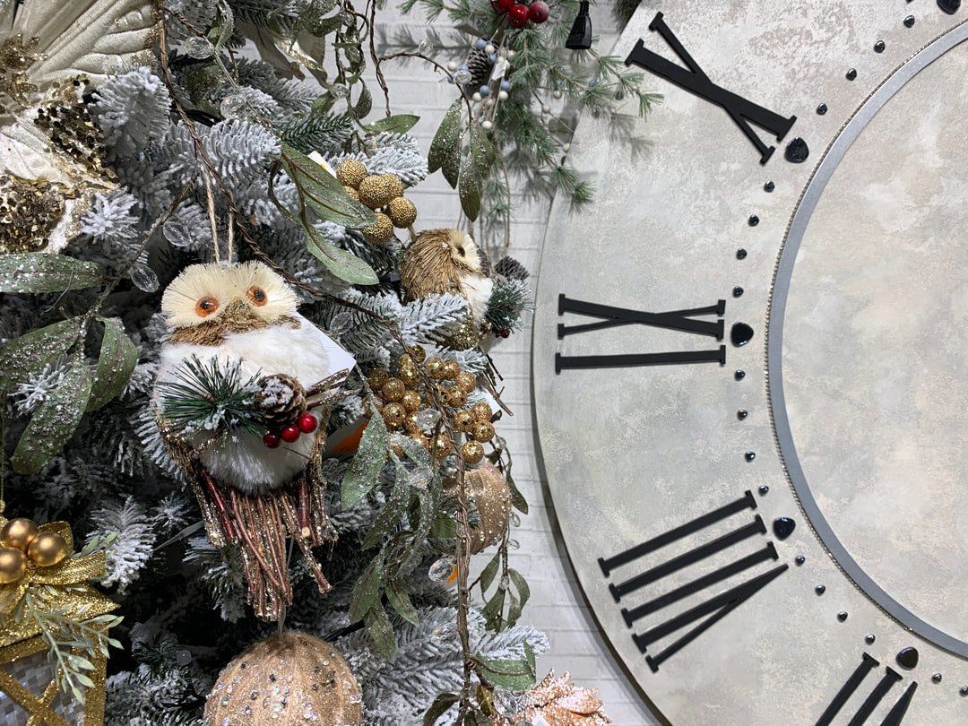 A large clock with roman numerals is sitting next to a christmas tree.