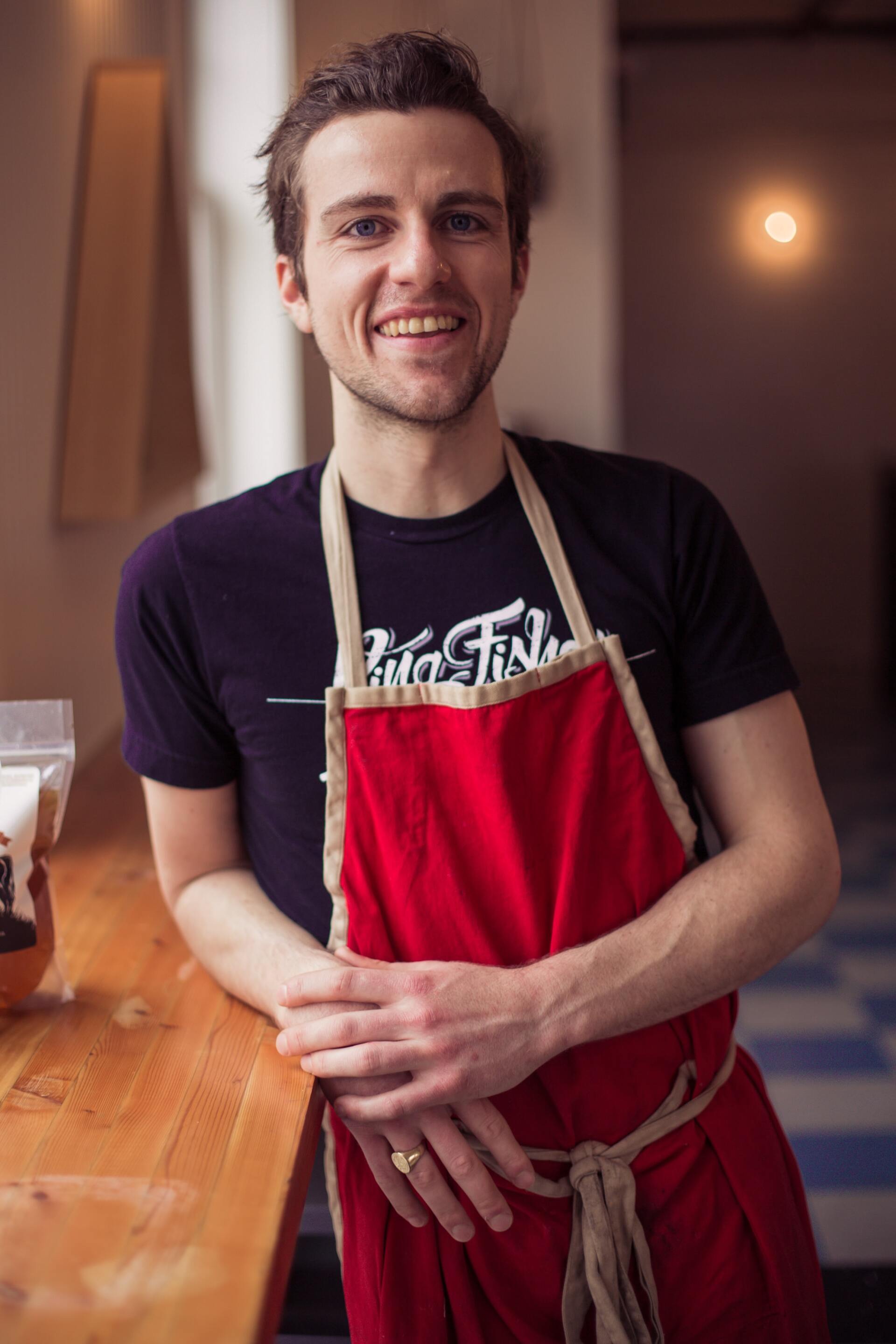 A man wearing a red apron and a purple shirt is standing in front of a counter.