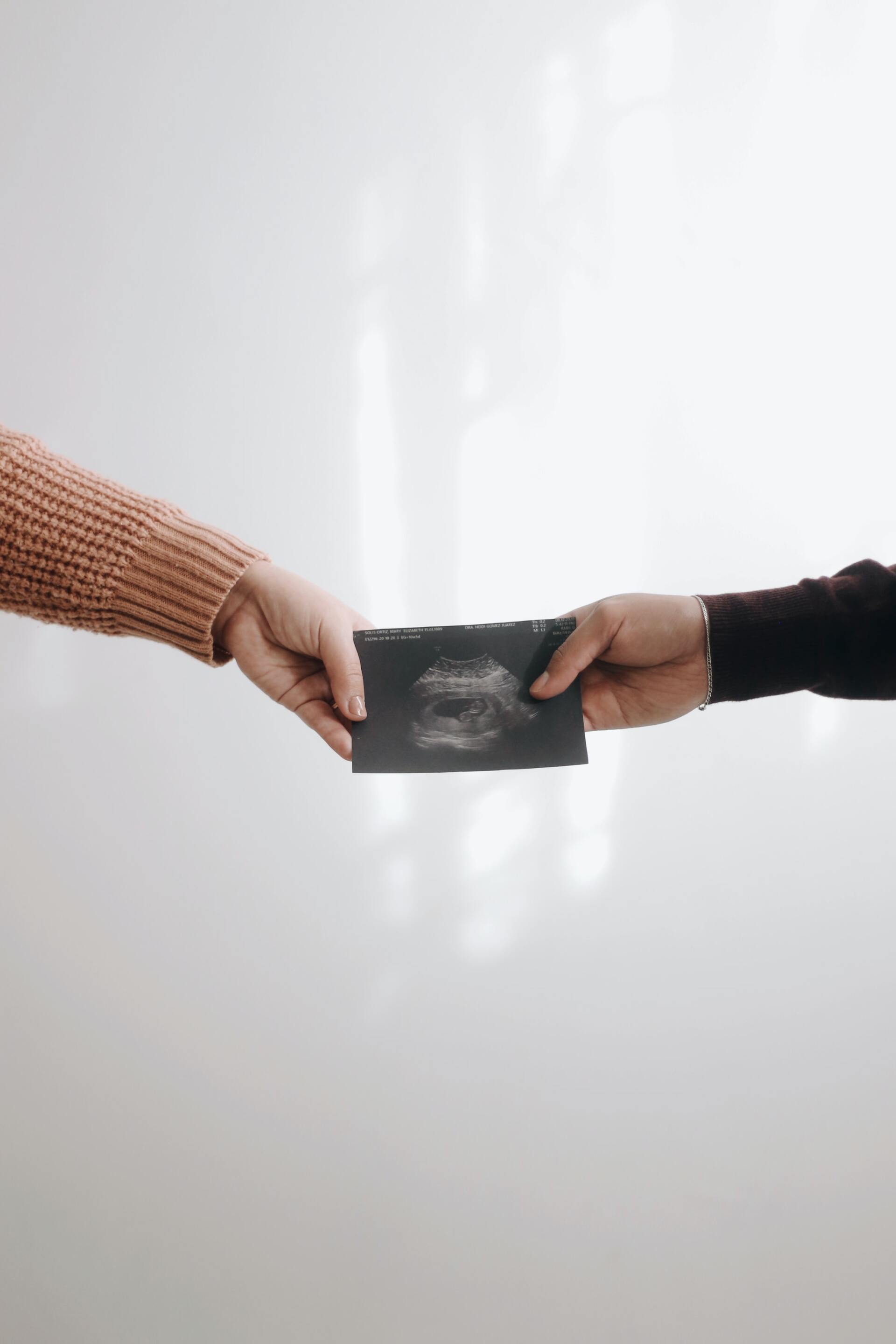 Two people's hands exchanging a dark square object, possibly a card or wallet, against a neutral background.