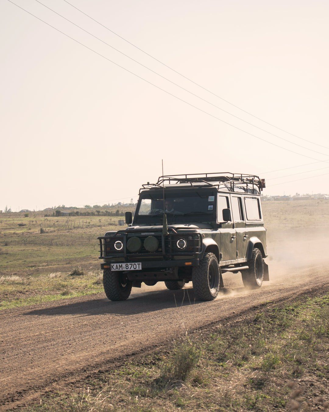 A jeep is driving down a dirt road in a field.