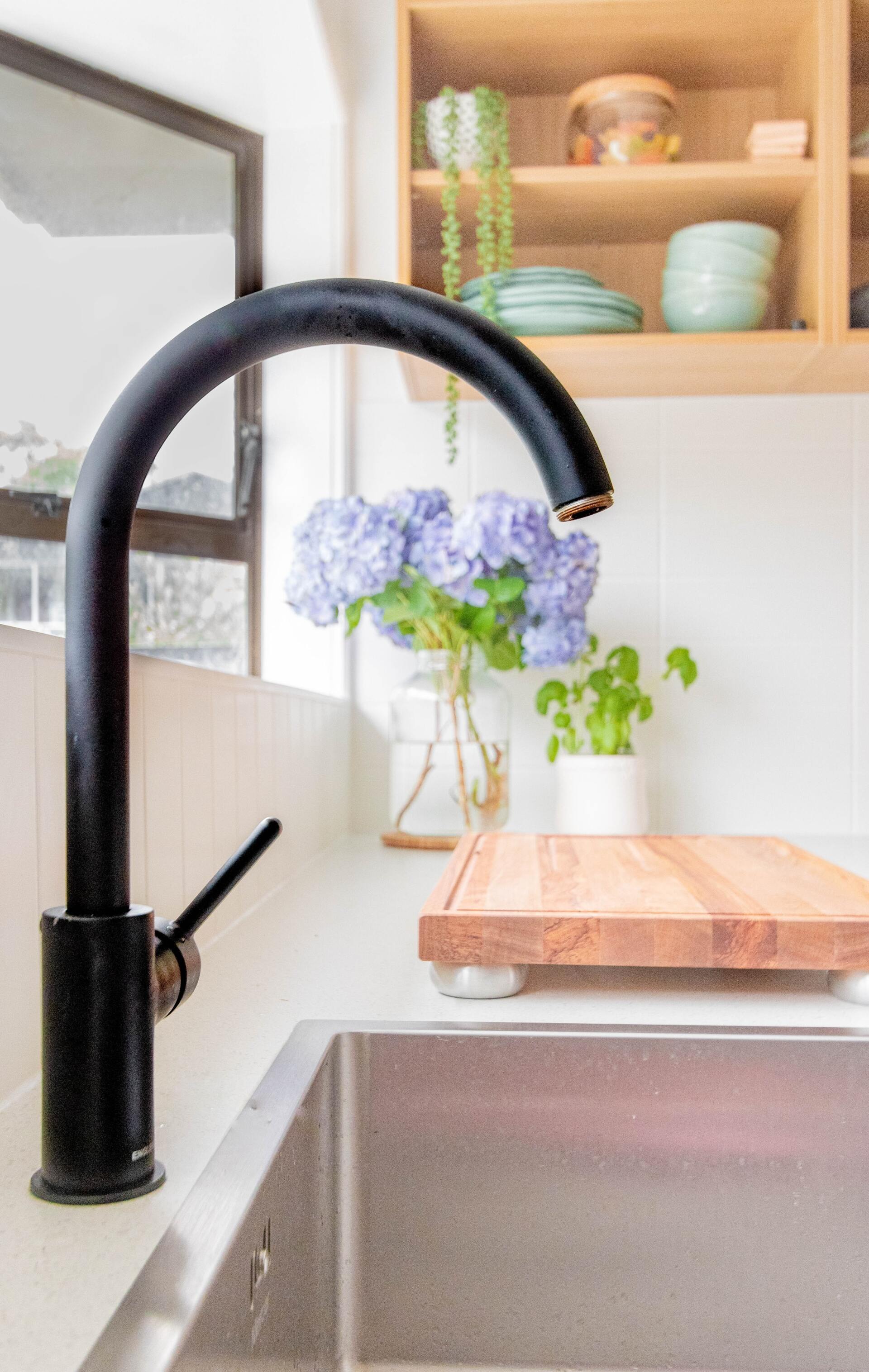 Black kitchen faucet over a stainless steel sink, with a bouquet of blue flowers.