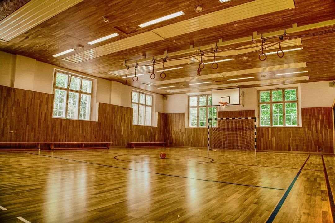 An empty gym with a wooden floor and a basketball hoop.