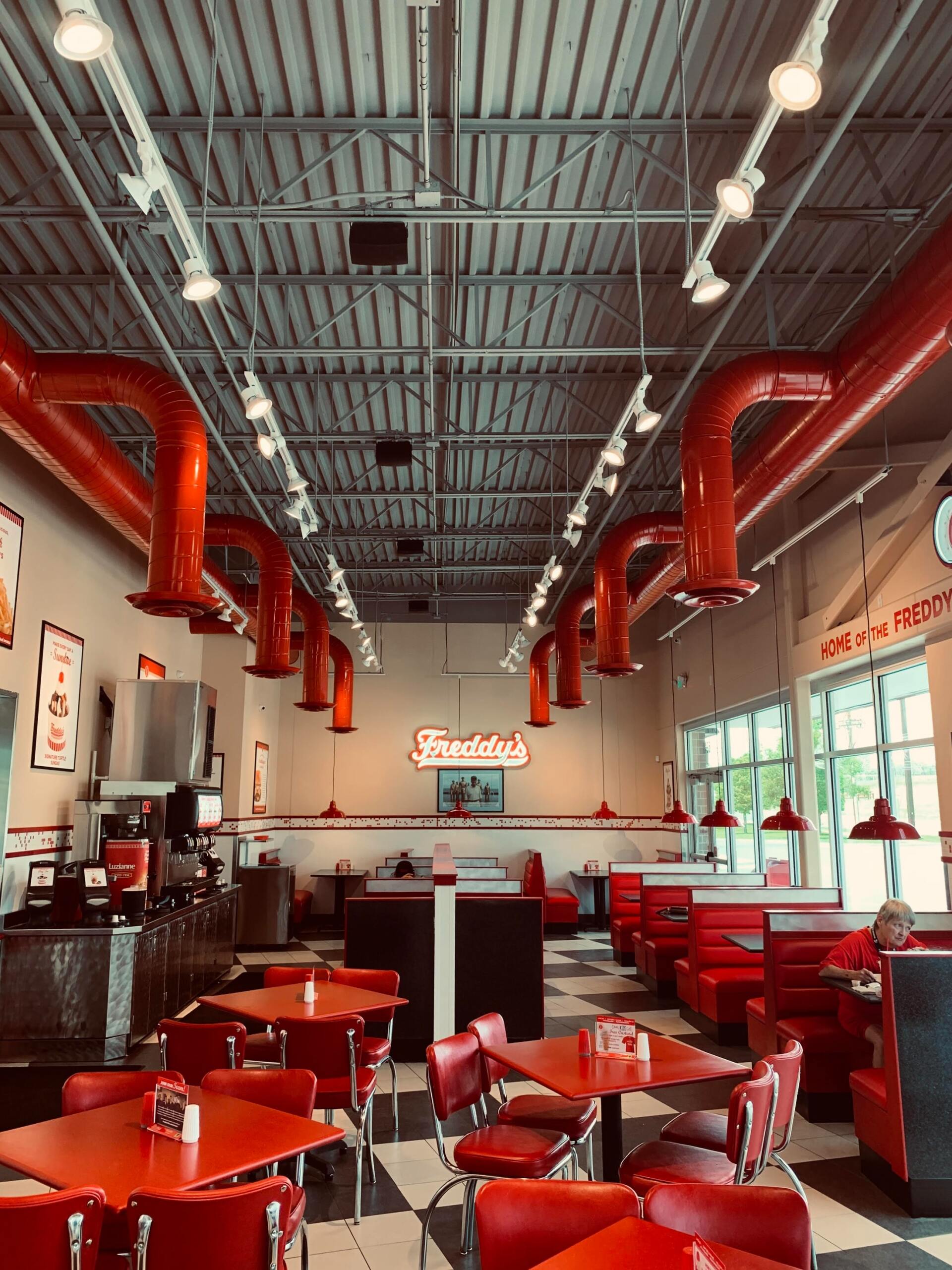 A diner with red tables and chairs and red pipes hanging from the ceiling.