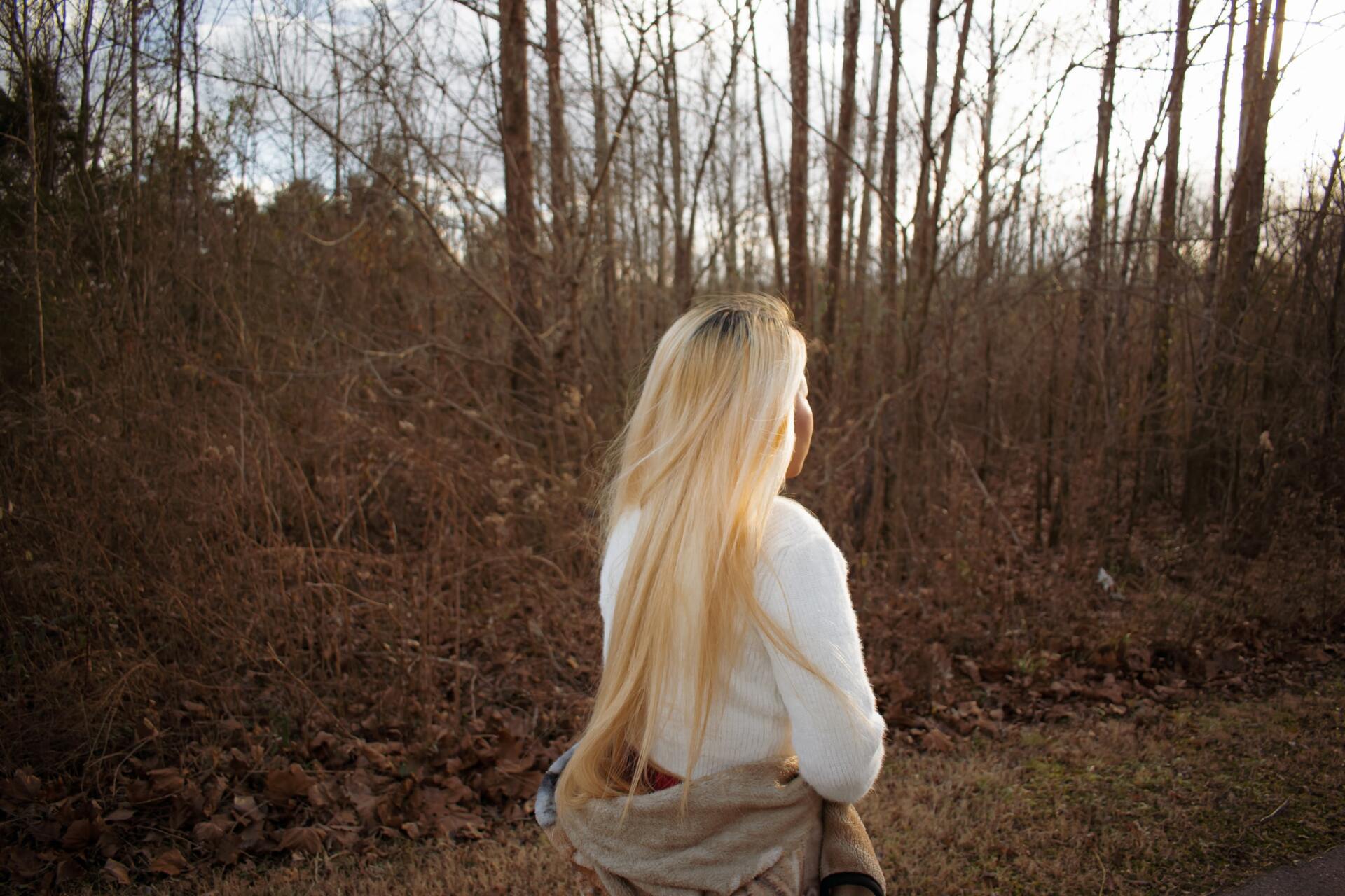 a woman with long blonde hair is standing in the woods