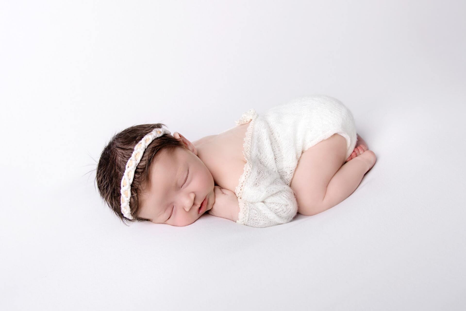 A newborn baby girl is sleeping on her stomach on a white surface.