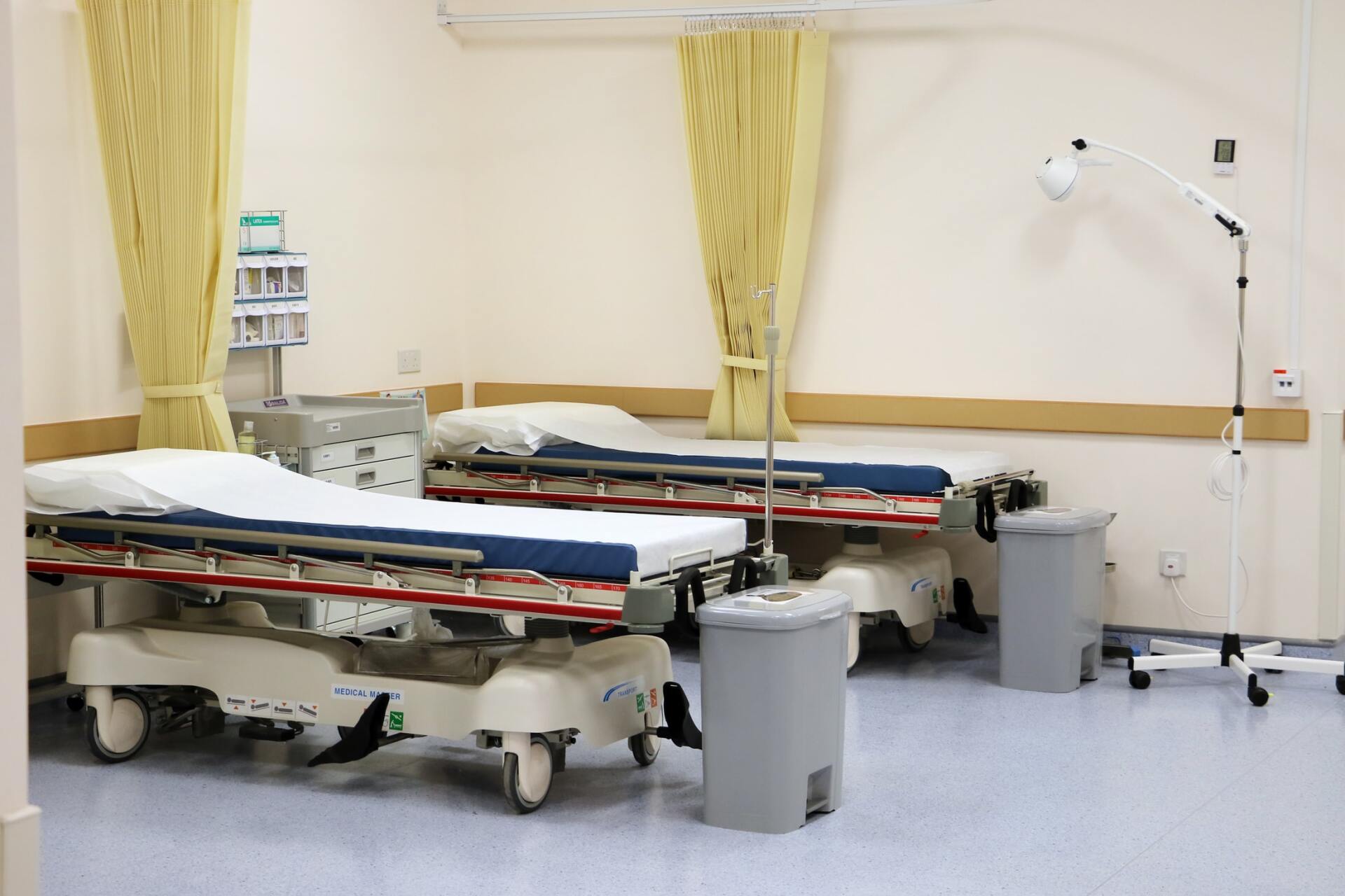 A hospital room with two stretchers and a trash can.