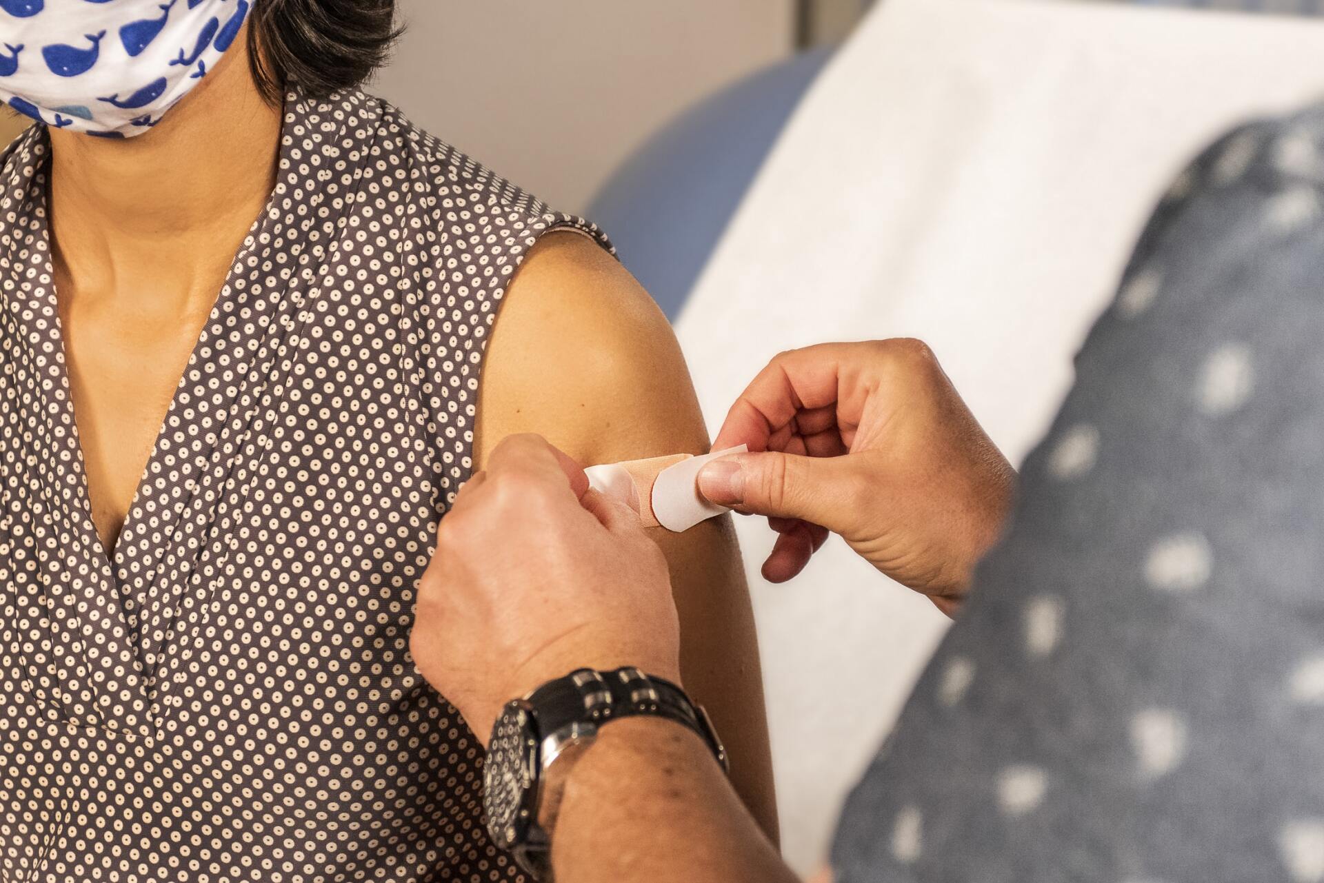 Image of a person applying a bandaid to a woman's shoulder, implying she has just received a vaccination.