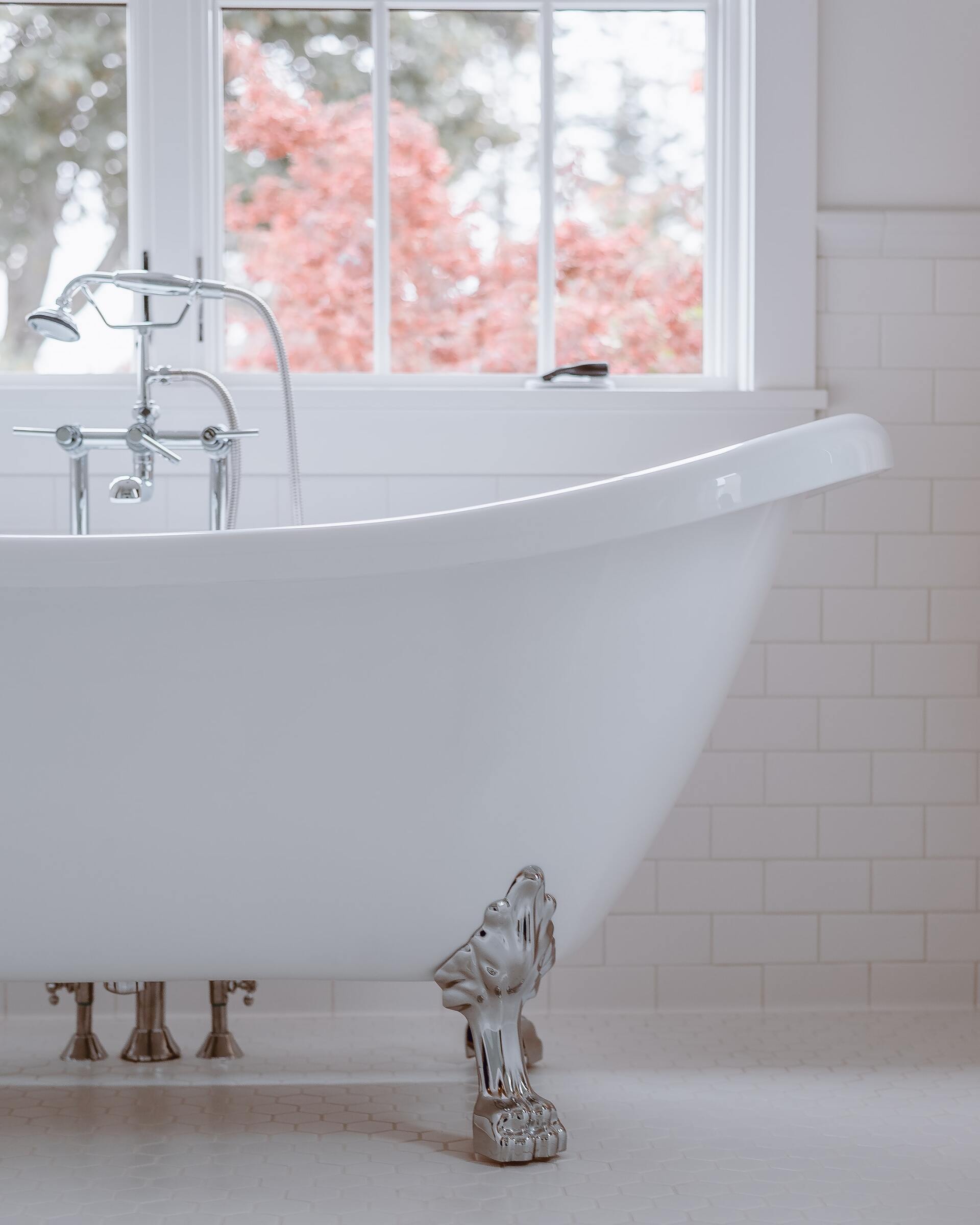 Clawfoot bathtub in a bright white bathroom with a window overlooking trees.