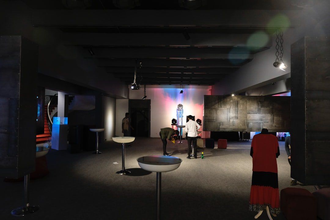 Um grupo de pessoas está de pé em uma sala escura com mesas e cadeiras.