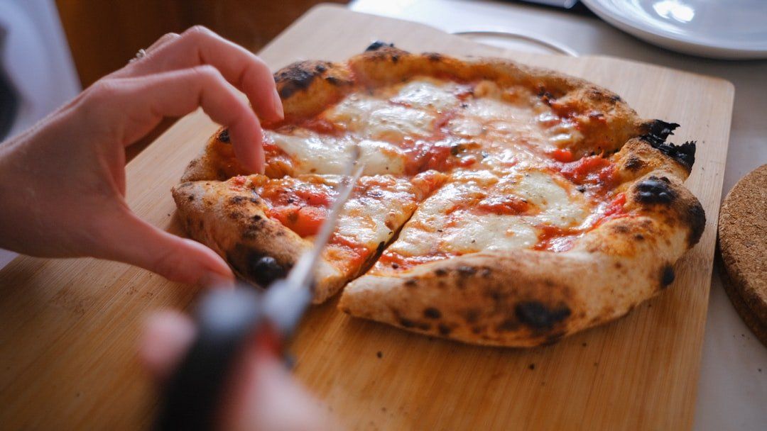A person is cutting a pizza on a wooden cutting board.
