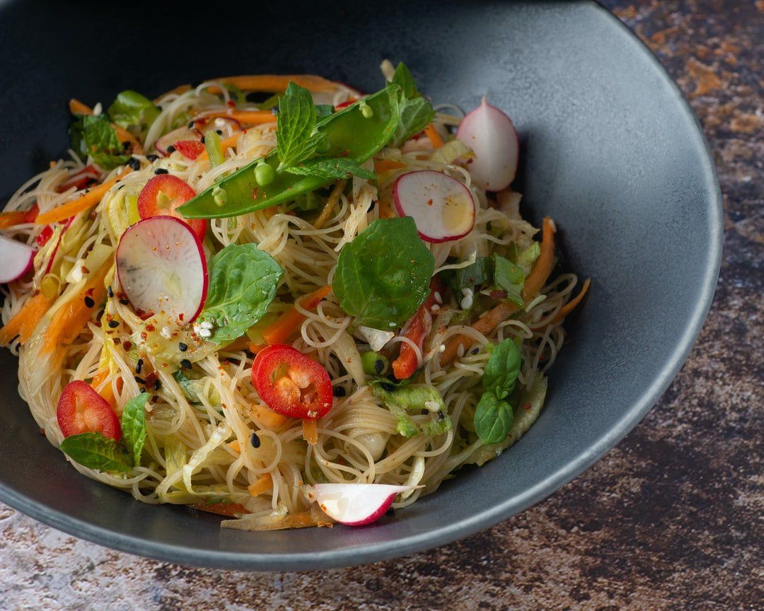A bowl of noodles with vegetables on a table.