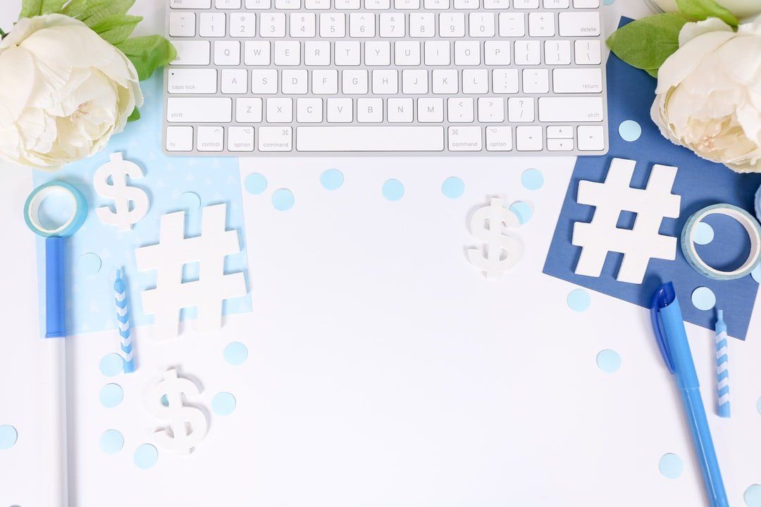 a desk with a keyboard , pens , flowers and hashtags on it .