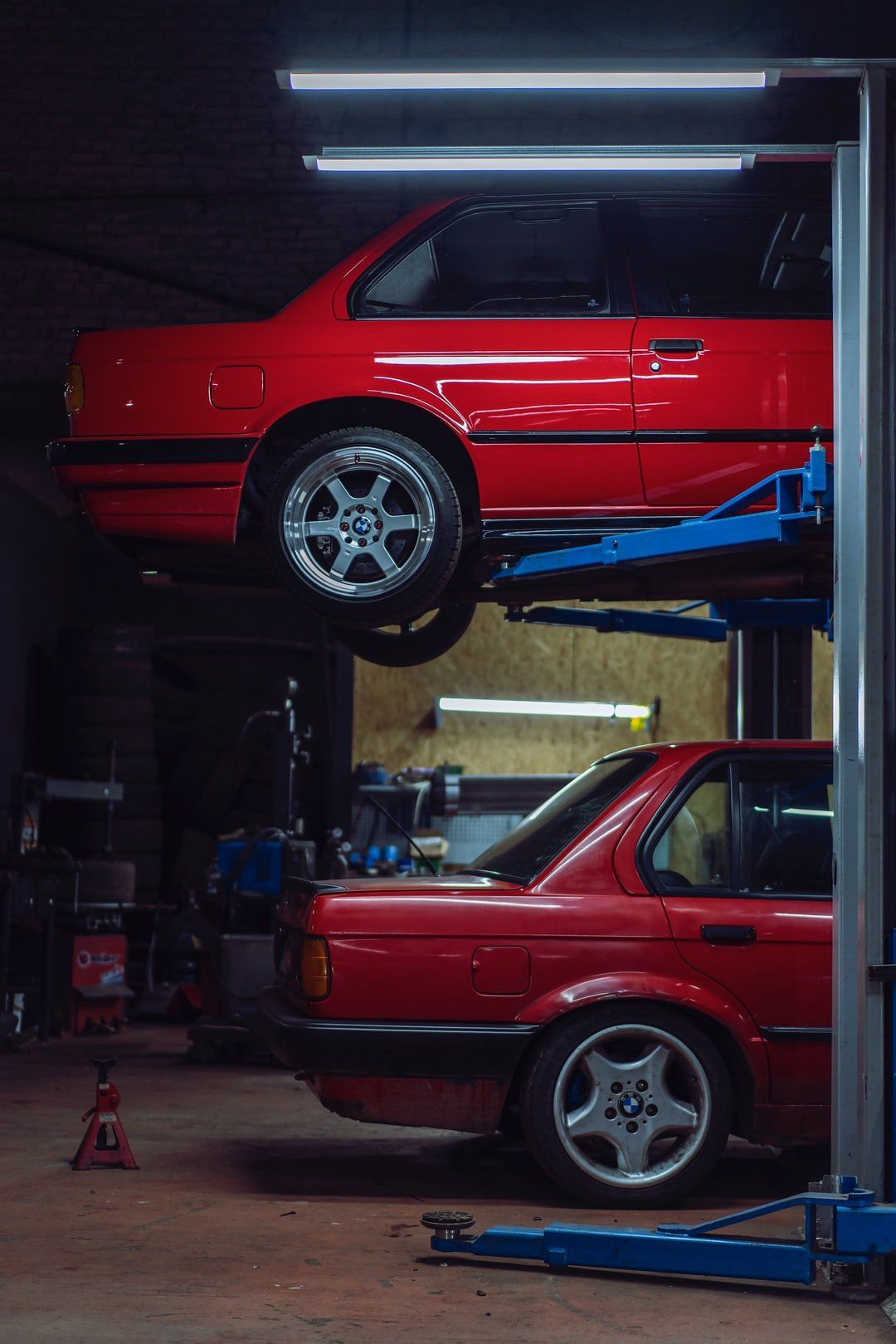 A red car is sitting on a lift in a garage.